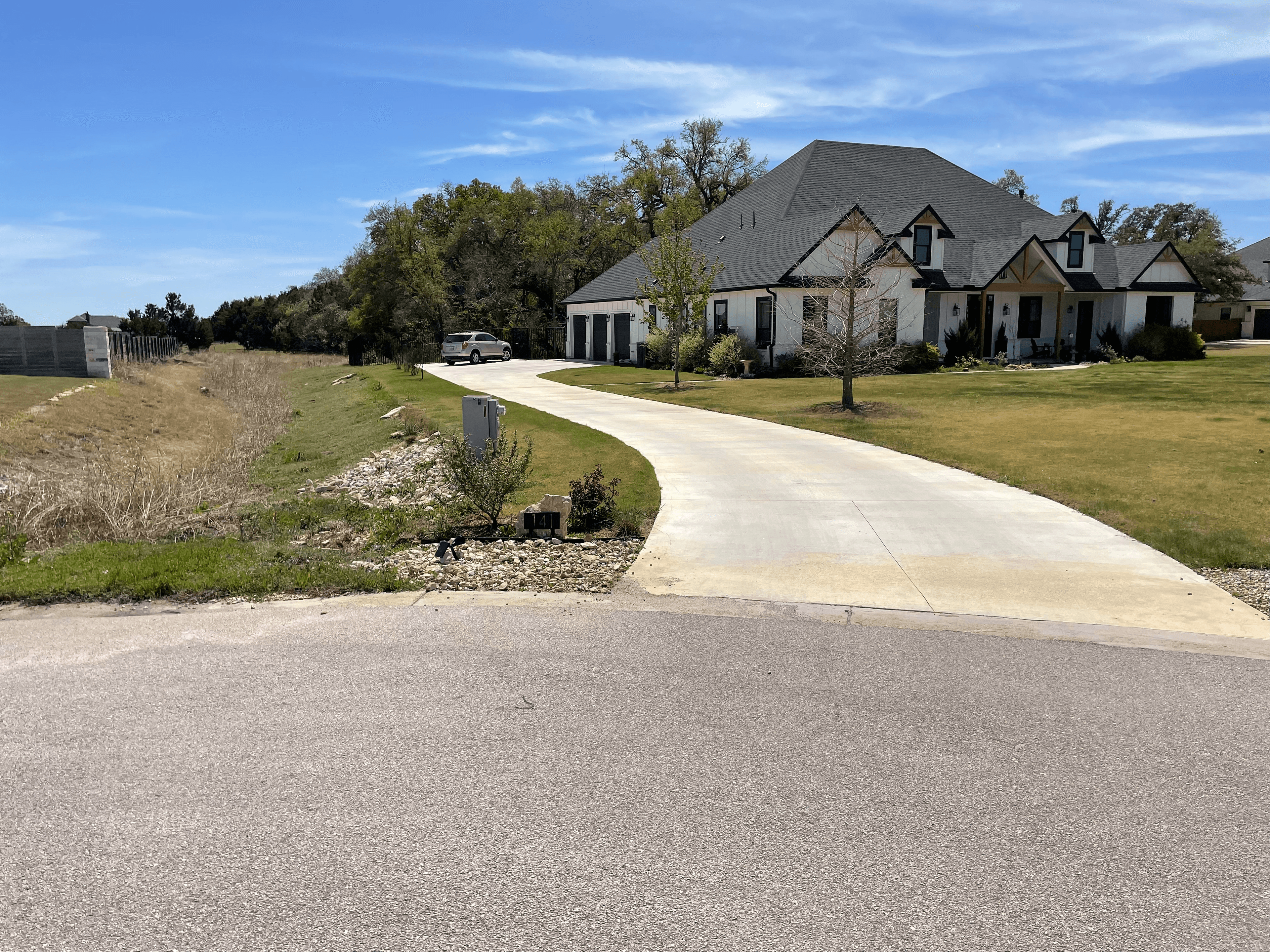 Modern white farmhouse with a dark roof and a long, curved concrete driveway.