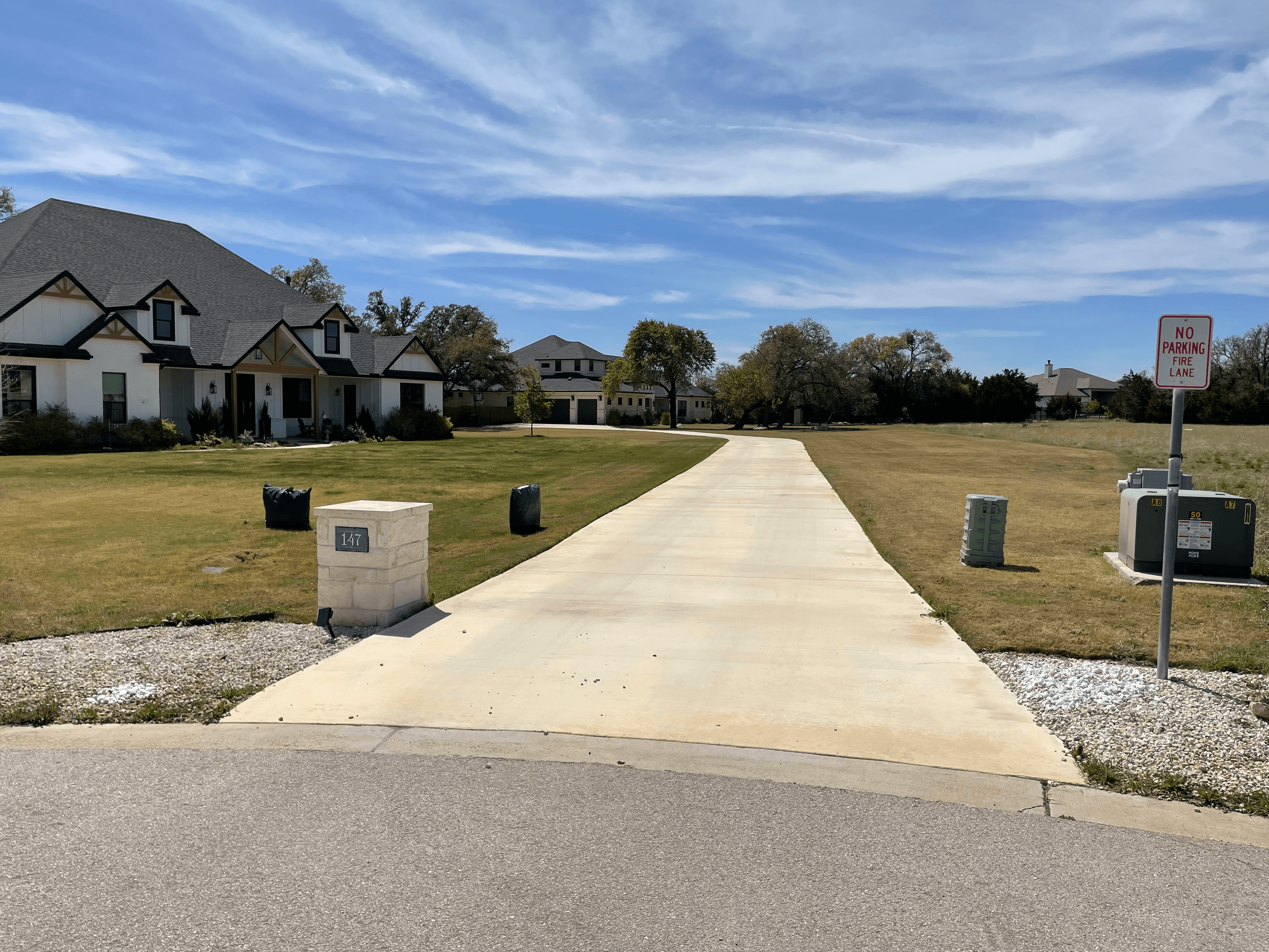 Long concrete driveway leading past a white house and stone mailbox under a blue sky.