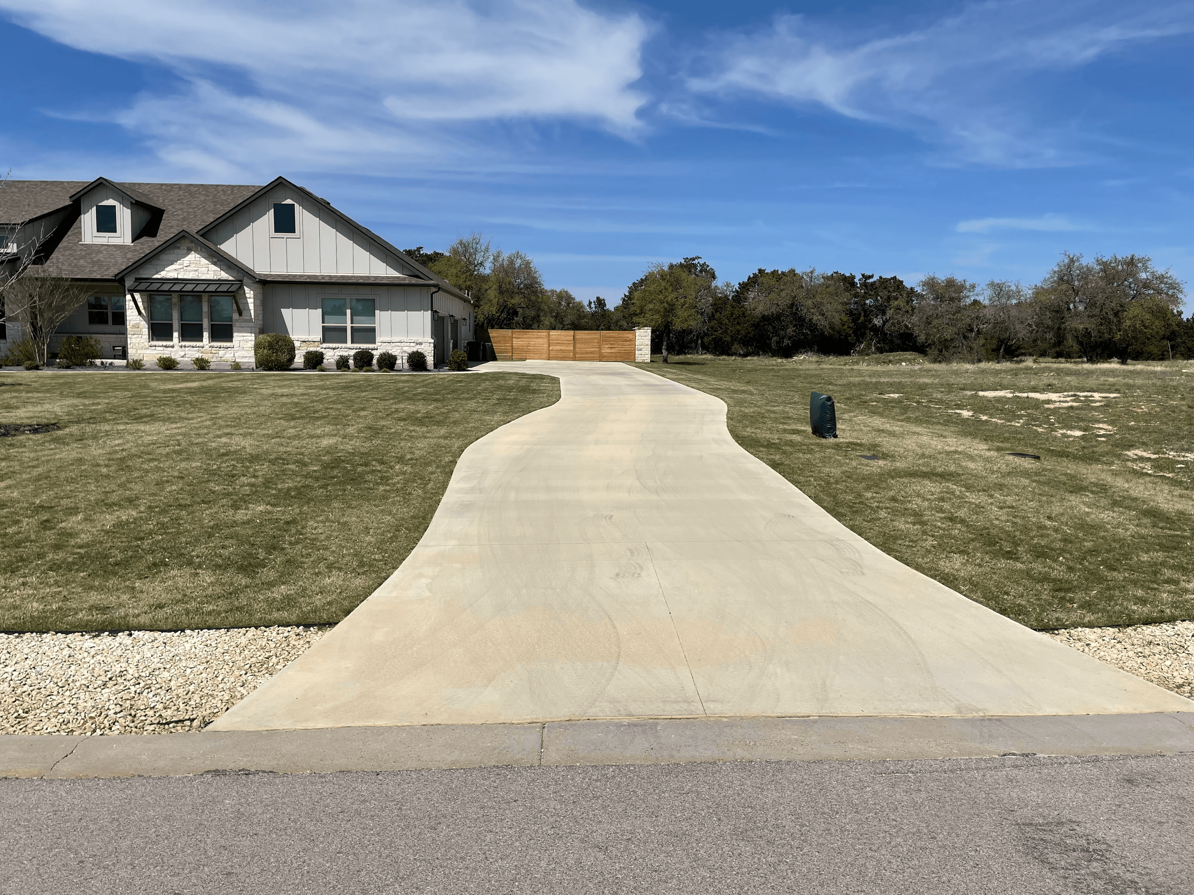 Long winding concrete driveway leading to a modern gray house under a blue sky.